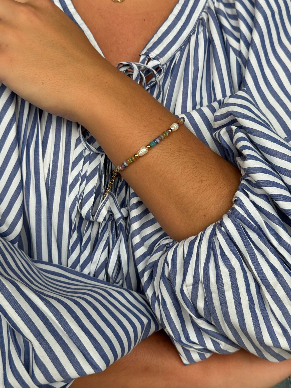 Ava Bracelet worn on the wrist – pastel stone beaded bracelet with pearls and a Gold Finished clasp, styled with a blue and white striped blouse