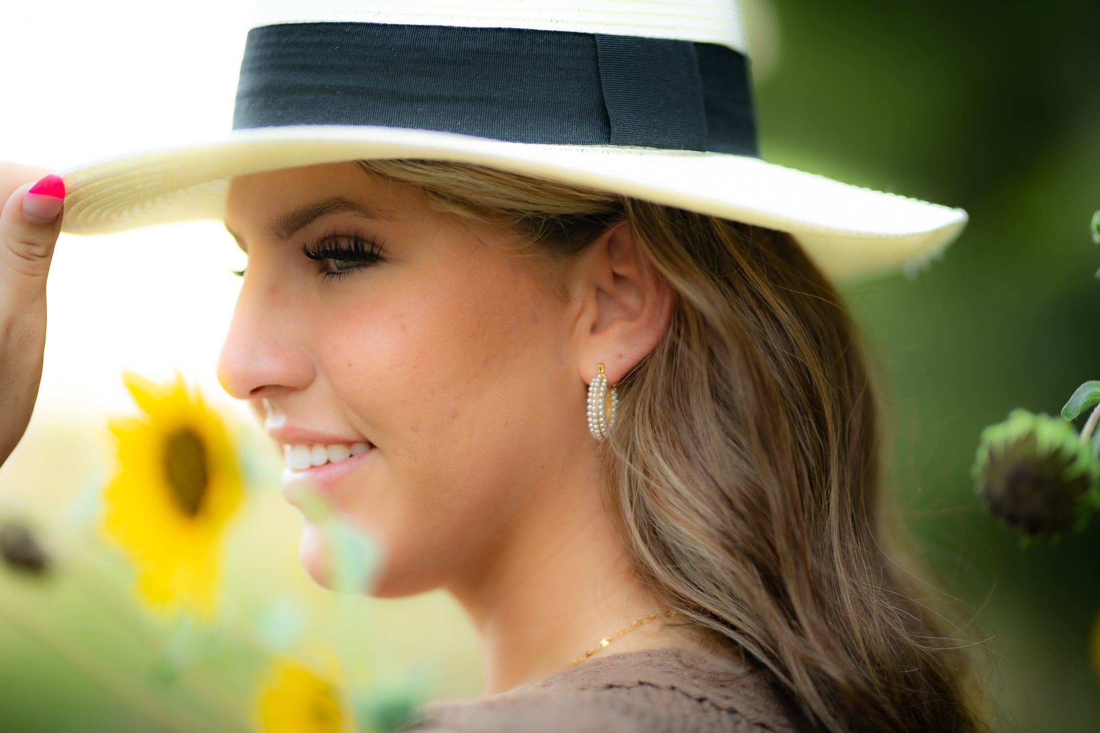 A woman in profile wearing a white wide-brim straw hat with a black band, photographed outdoors near blurred yellow flowers.