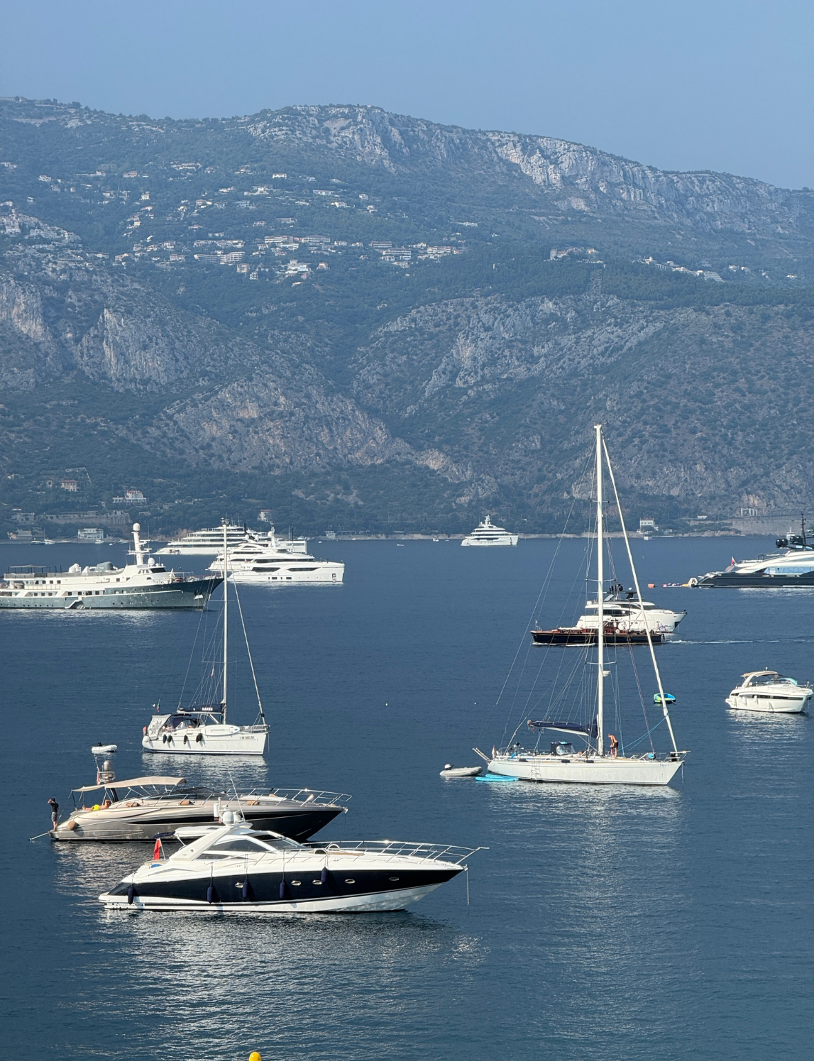 Yachts and sailboats on a calm blue sea with mountains in the background near Monaco.