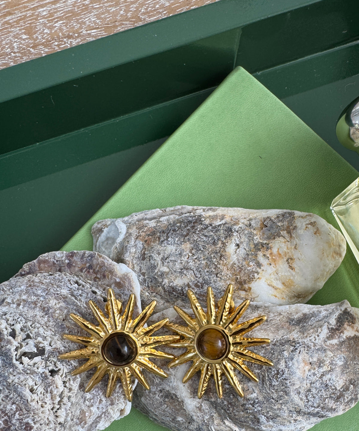 Gold sun-shaped earrings on a textured stone surface with a green background