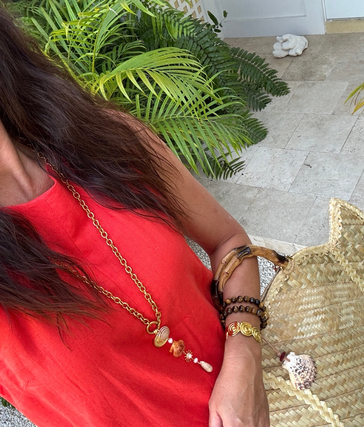 Person wearing a red top with a gold necklace and bracelets, standing outdoors.