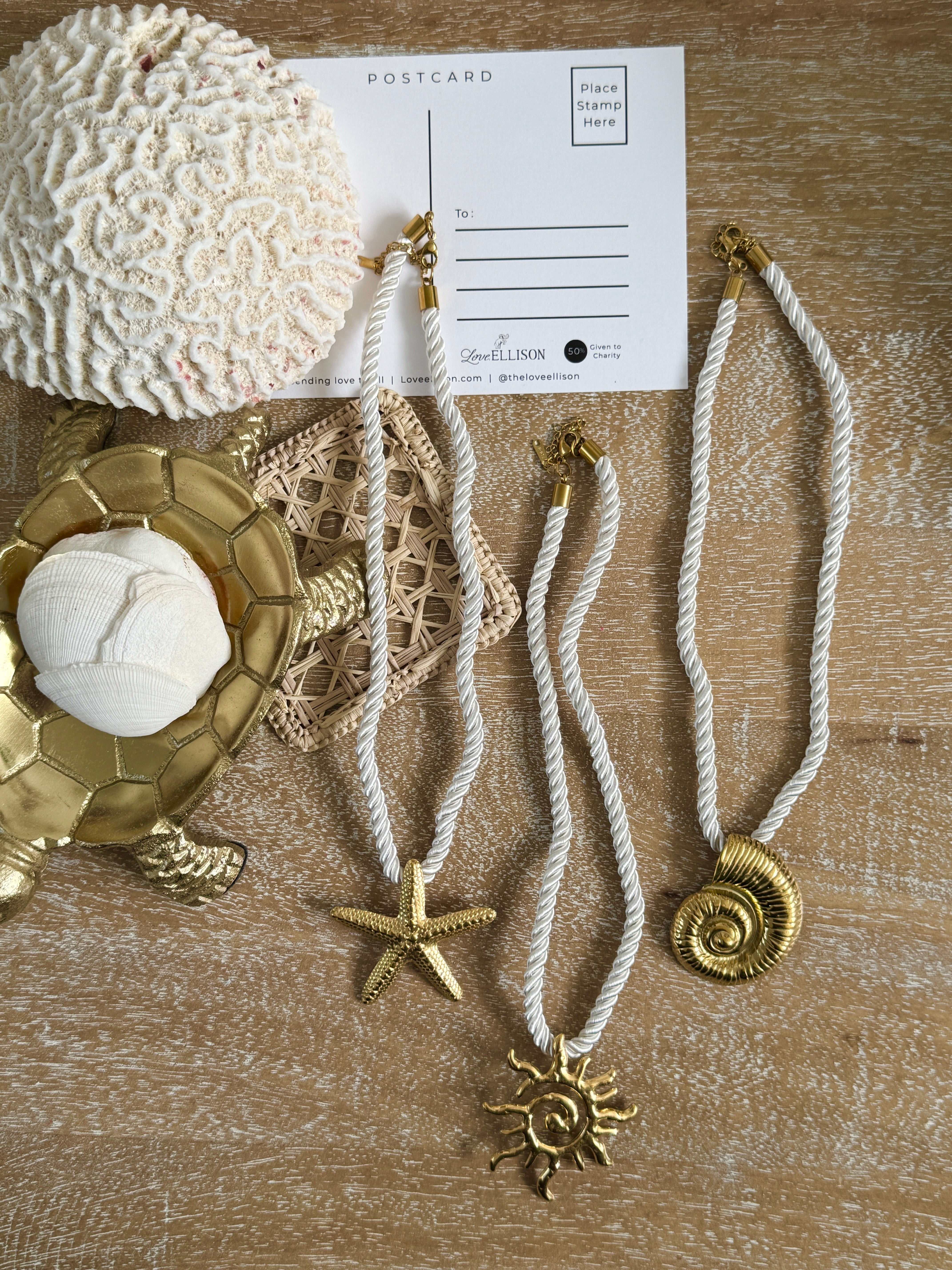Necklaces with starfish and shell pendants on a textured surface with a postcard.