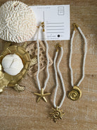 Necklaces with starfish and shell pendants on a textured surface with a postcard.