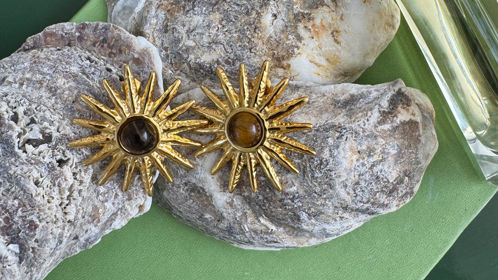 Gold sun-shaped earrings on a textured stone surface with a green background