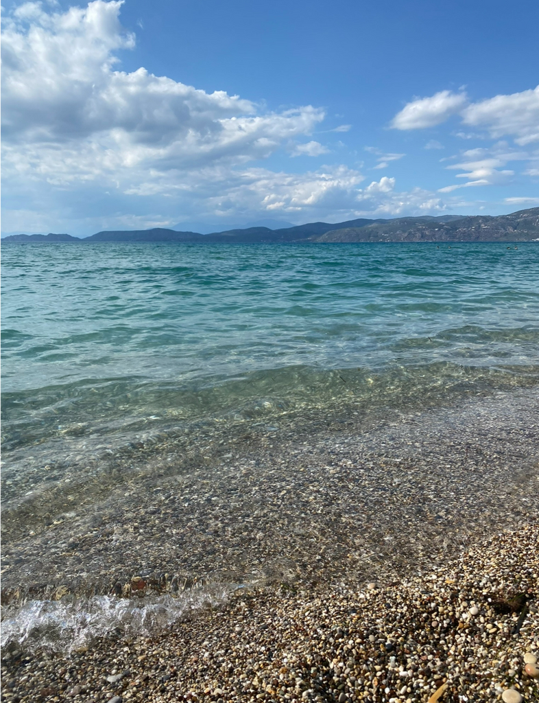 Relax at Kalamia Beach in Corinth, known for its clear waters, palm trees, and peaceful vibe.