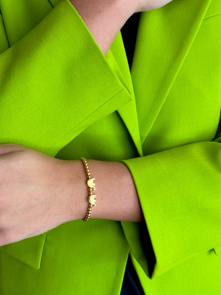 A close-up of a person's wrist wearing a delicate gold chain bracelet with two elephant charms, styled with a bright lime green blazer.