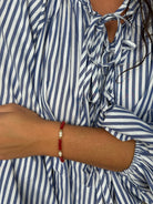 Lara Bracelet worn on the wrist – red beaded bracelet with pearl accents, styled with a blue and white striped blouse