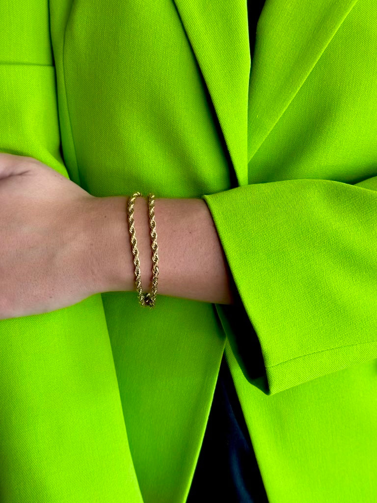 A close-up of a person's wrist wearing two thin gold chain bracelets, styled with a bright neon green blazer.