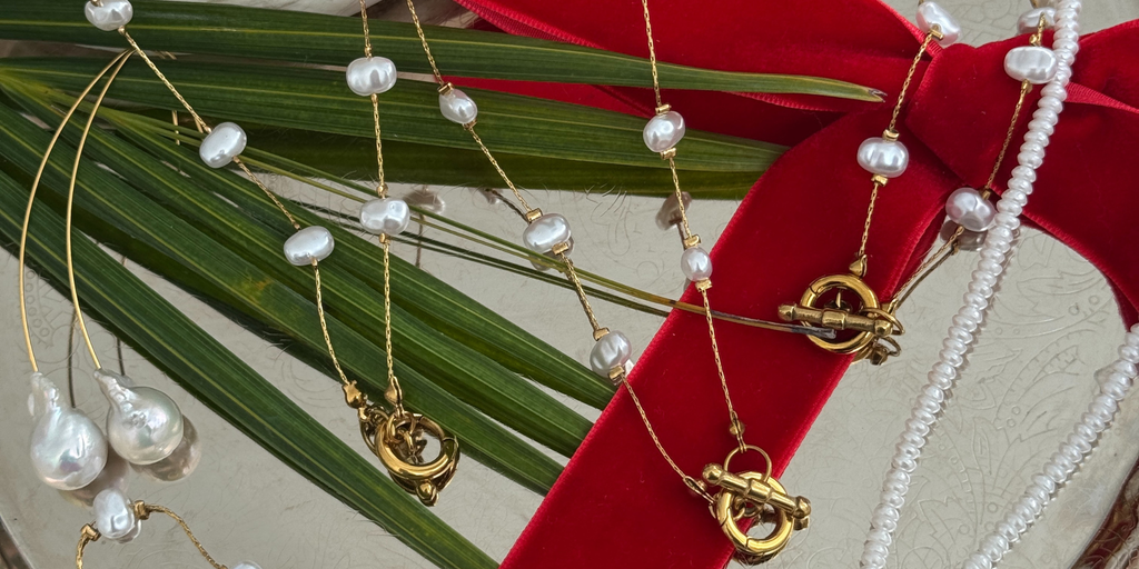 Gold jewelry with pearl accents on a red ribbon against a green leaf background