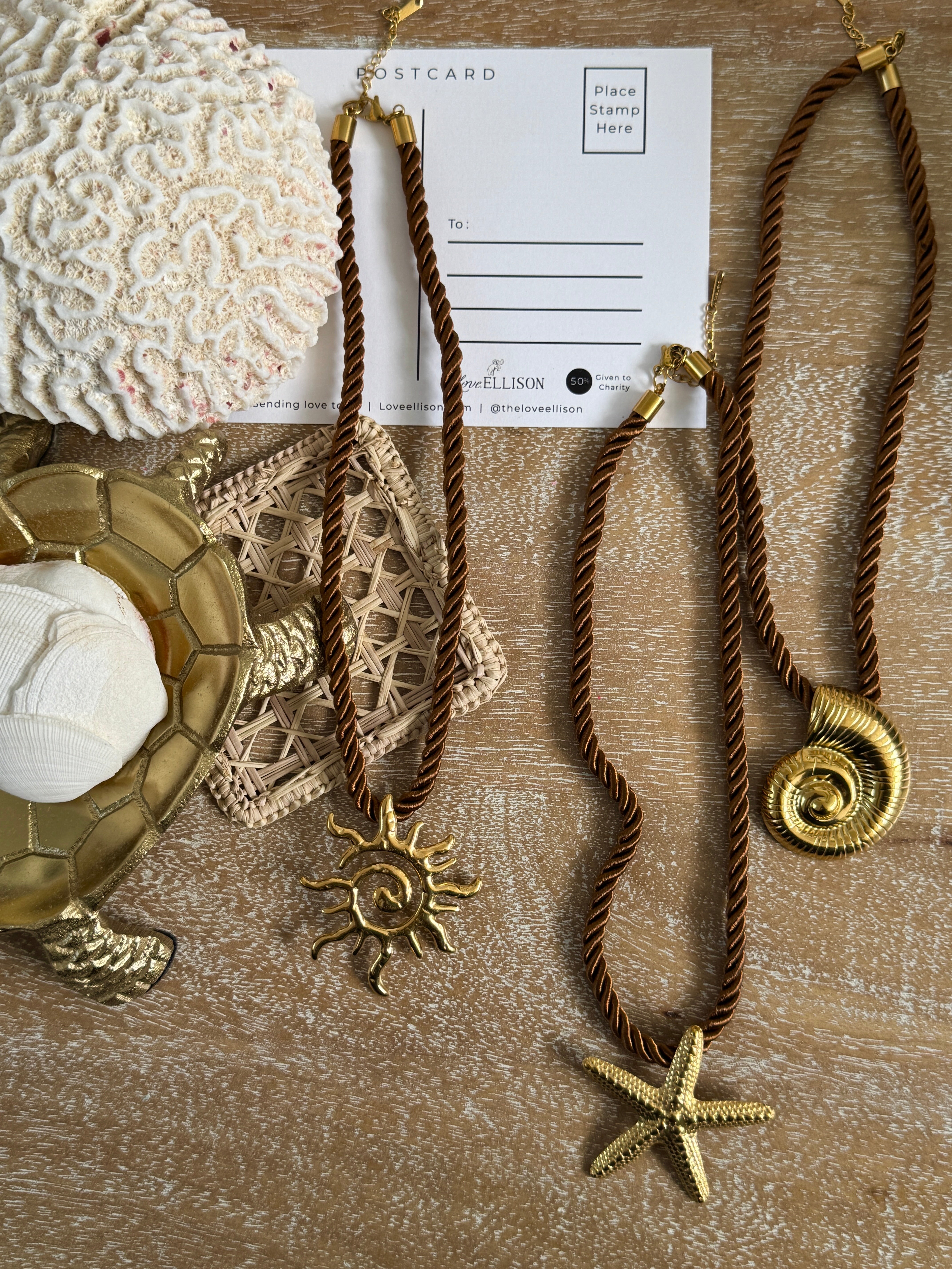 Brown rope necklace with gold starfish and sun pendant on a textured surface