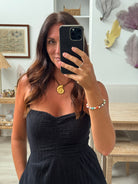 Person taking a mirror selfie with a phone, wearing a black dress and gold earrings.