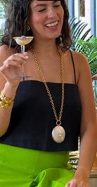 Woman holding a cocktail with a long gold necklace and green skirt.