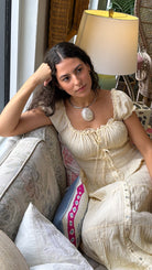 Woman in a white dress sitting on a couch with a shell pendant necklace.