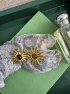 Gold sun-shaped earrings on a textured stone surface with a green background