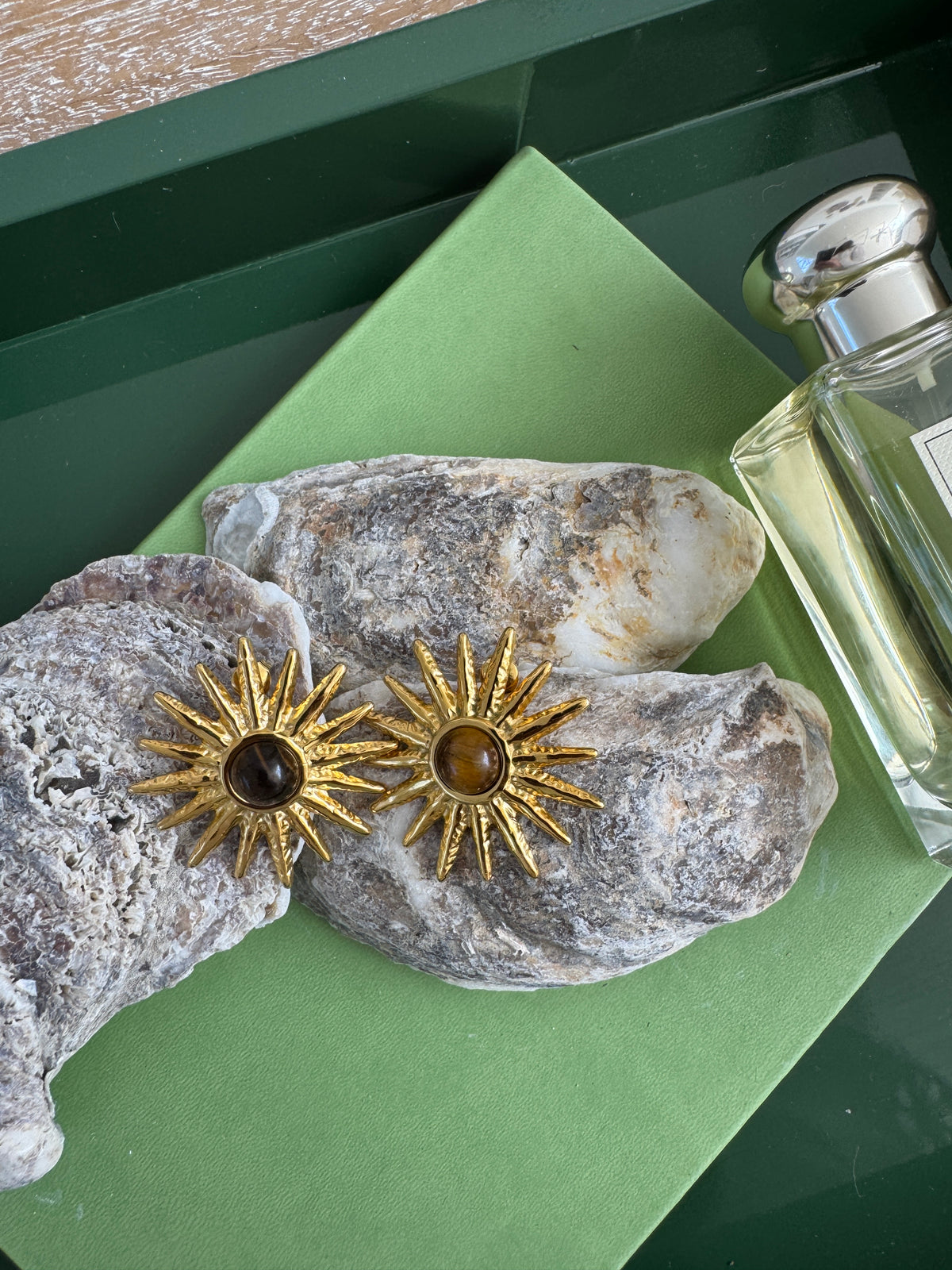 Gold sun-shaped earrings on a textured stone surface with a green background