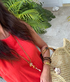 Person wearing a red top with a gold necklace and bracelets, standing outdoors.
