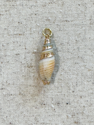 Shell-shaped pendant with a gold chain on a textured beige background